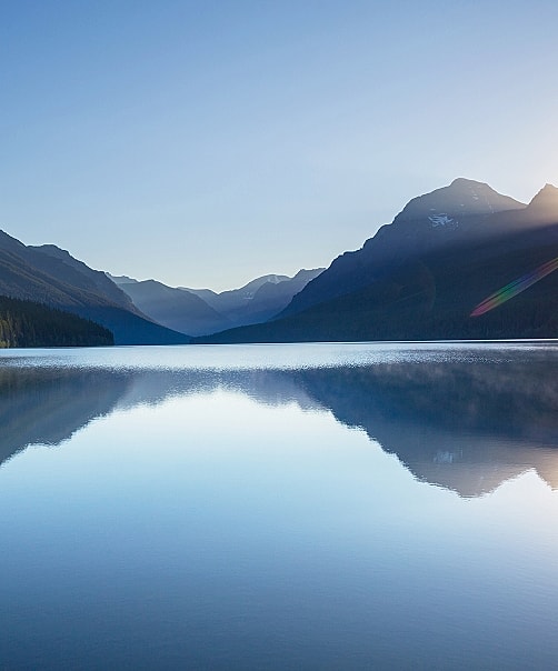 Serene lake reflecting mountains at sunrise.