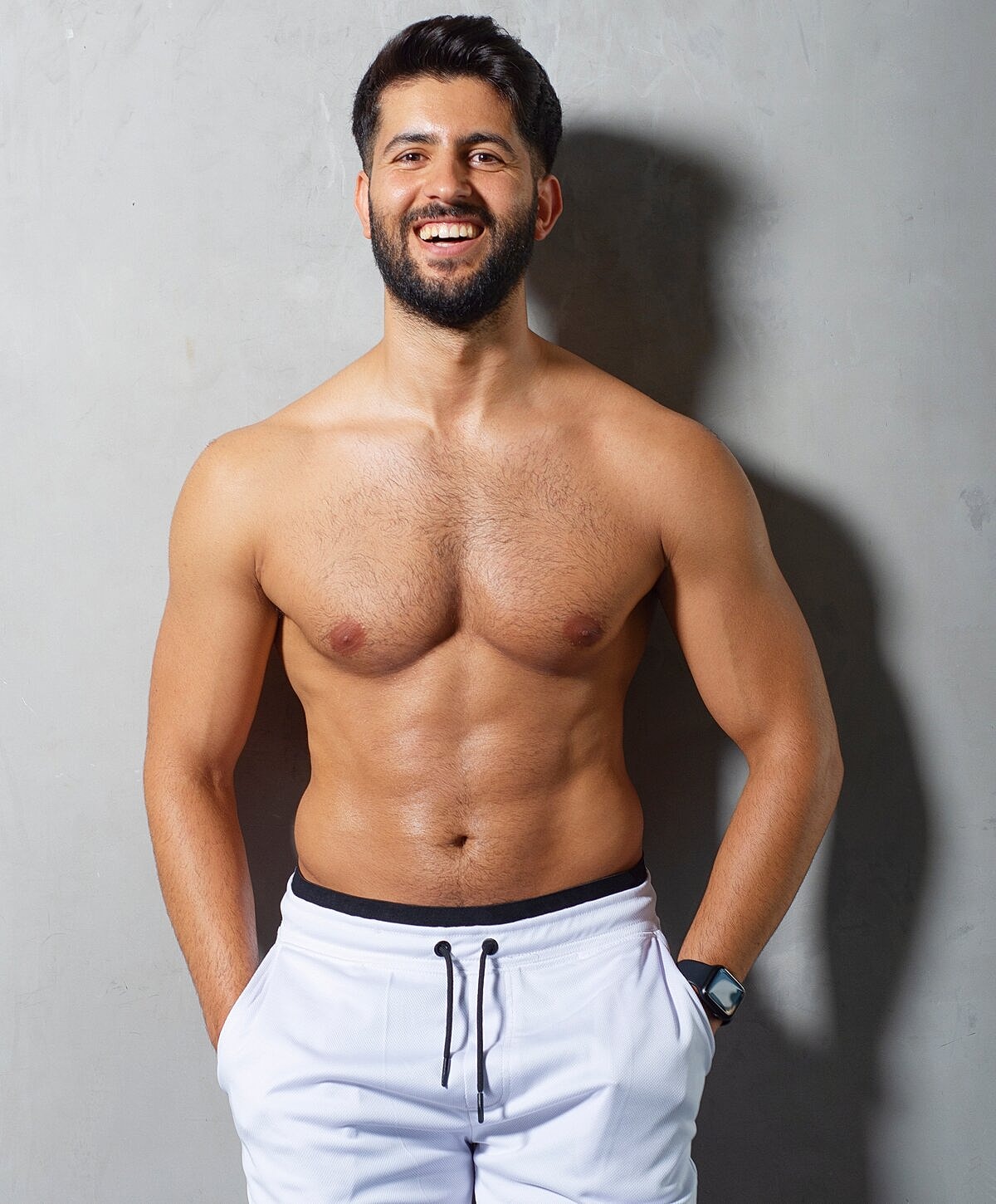 Smiling man posing shirtless against gray background.