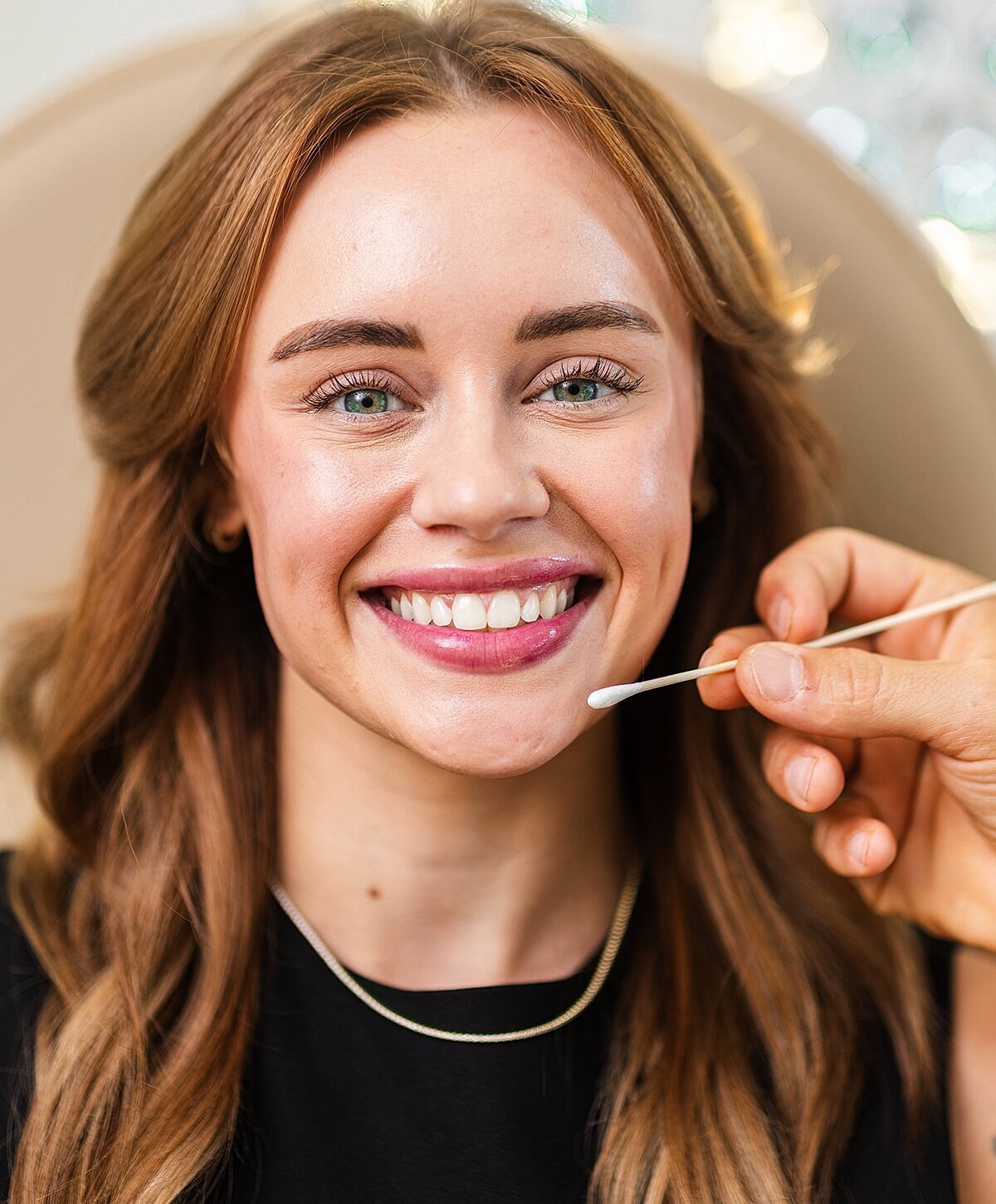 Woman smiling during makeup application process.