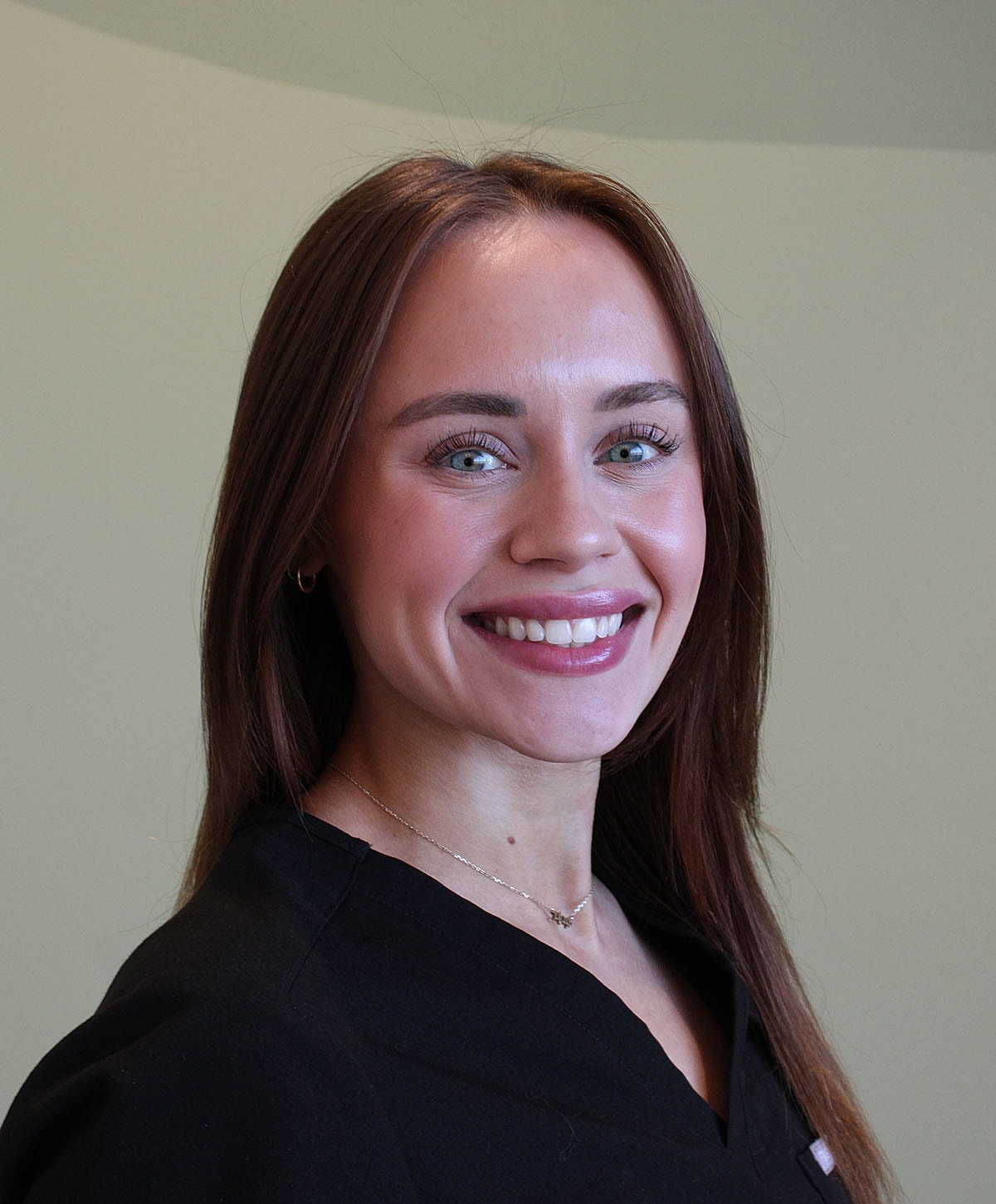 Smiling woman in black attire against neutral background.