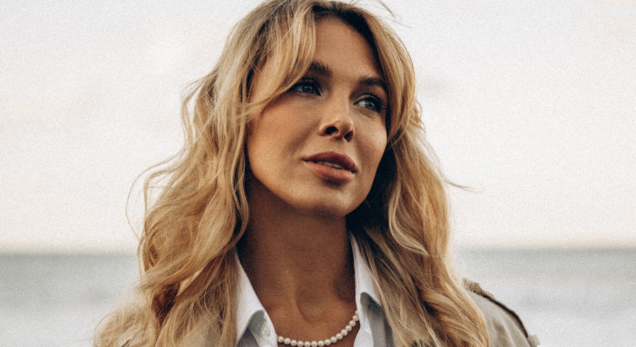 Woman with blonde hair by the beach.
