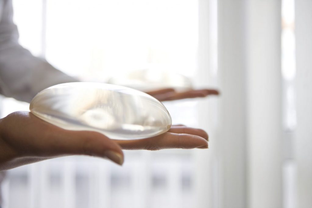 Side view of hands holding breast implants.