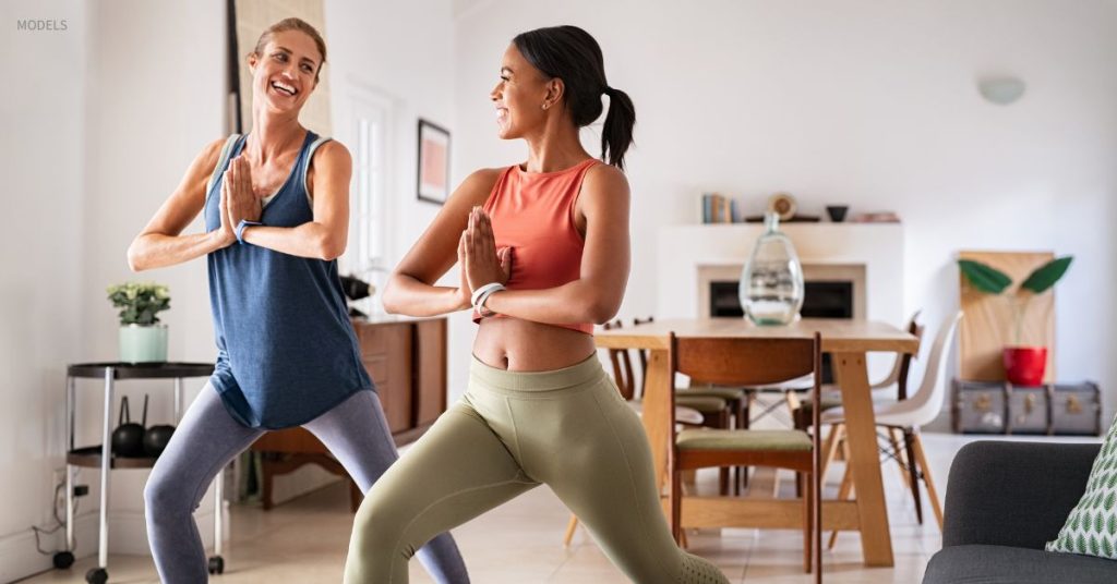 Two athletic-looking women (models) doing yoga indoors.