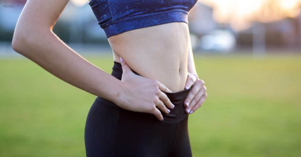 Woman with a flat stomach (model) resting hands on her hips outdoors.