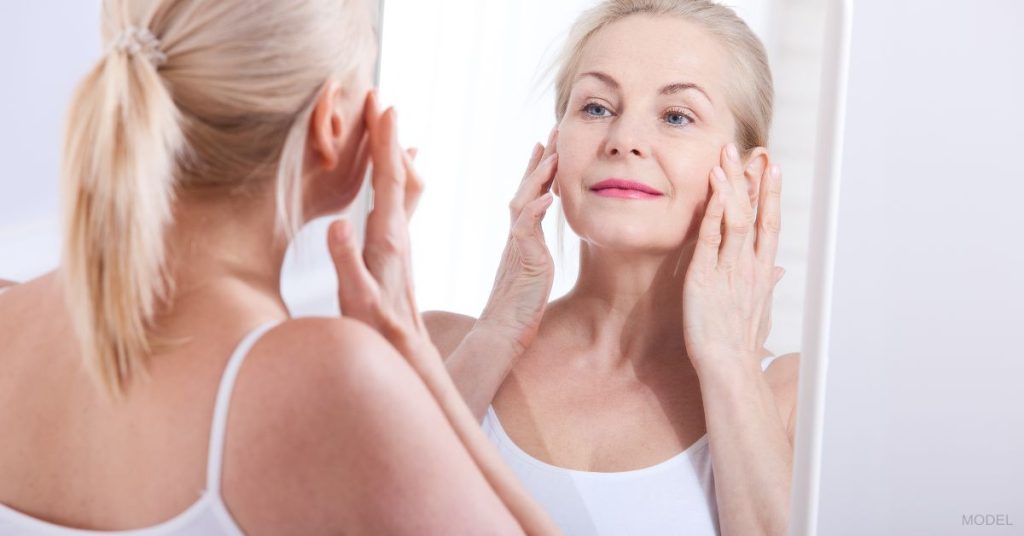 Mature woman (model) checking her eyes in the mirror to look for scarring after blepharoplasty.